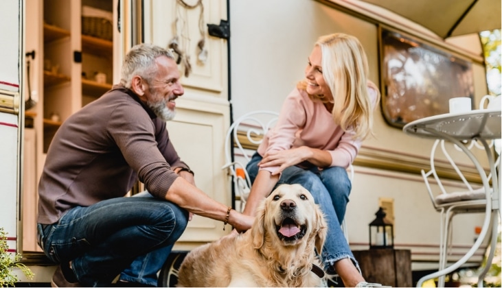A smiling couple with thier golden retriever bonding together outside their Bunkhouse Travel Trailer in Apache Junction, AZ